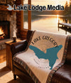Tapestry throw blanket featuring Lake Gregory silhouette and compass on a leather couch.