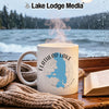 White mug with Flathead Lake, Montana design, steam rising, by a window.