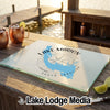 A glass cutting board featuring a blue map of Lake Marion with a compass rose design rests on a wooden dock with drinks.
