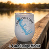A white travel tumbler featuring a blue lake map and compass design sits on a wooden dock at sunset.