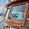 Turquoise Wourika Life sticker on polished wooden boat window with "Lake Lodge Media" text.