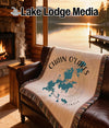 Fringed throw blanket with Chain O'Lakes map design on leather sofa by fireplace.