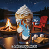 Glass of drink with whipped cream, campfire, lake, and s'mores ingredients.
