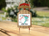 Sled ornament with text "Merry Christmas FROM Lake Waco" hangs on twine.