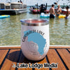 A white insulated wine tumbler featuring a Garibaldi Lake map graphic rests on a wooden dock with people swimming in the lake behind it.