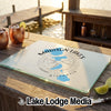 A glass cutting board featuring a Madison Lakes Wisconsin map and compass design on a wooden table.