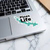 "Pines Life" sticker with lake shape on a laptop keyboard.