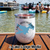 A white stainless steel insulated tumbler with a Lake Arrowhead map graphic rests on a wooden boat deck with people swimming in the lake background.