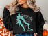 Black crewneck sweatshirt with a teal map outline and compass rose.