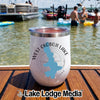 A white insulated tumbler with a compass graphic and West Okoboji Lake text on a wooden surface near water.