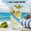 A glass of bubbly drink with lime and mint on a beach with a sailboat.
