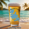Glass of beer with Lake Chaubunagungamaug map and compass design on beach.