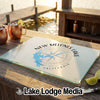 A rectangular glass cutting board featuring a New Melones Lake map design rests on an outdoor wooden table.