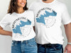 White t-shirts featuring a blue map of Merrymeeting Lake and compass design labeled New Hampshire.