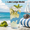 Glass with beverage, limes, and mint garnish on a beach with sailboat in background.
