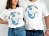 Two white t-shirts featuring a blue outline of Broadway Lake and a compass rose graphic.