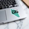 Teal sticker on laptop with "Mohave Life" text and small copyright notice.