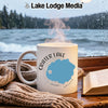 White mug with "Crater Lake Oregon" design next to a book and scarf.