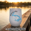 A white tumbler with a blue map of Spoon Lake, Illinois, sits on a wooden dock at sunset.