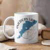 White mug with blue American Lake map graphic and compass, steam rising.