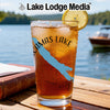 Glass of iced tea with "Camas Lake" and compass design, set by a lake.