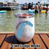 A white insulated wine tumbler with Grand Lake Colorado text sits on a wooden dock near a lake.