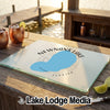 A glass cutting board featuring a blue map of Newnan's Lake, Florida, sits on a wooden table outdoors.