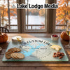 A personalized glass cutting board with a map design sits on a wooden table, surrounded by appetizers.