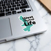 Teal West Okoboji Life sticker on a laptop keyboard over a marble surface.