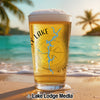 Glass of beer with a lake map and compass design on a beach.