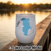 A white travel tumbler featuring a blue outline of Lake Piru rests on a wooden dock at sunset.