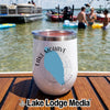 A white insulated wine tumbler with a Lake Mohave Arizona graphic stands on a wooden boat deck with people swimming in the lake.