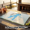 A rectangular glass cutting board featuring a blue map of Lake Dillon, Colorado rests on a wooden dock with copper mugs.