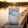 A white travel tumbler with a blue map of Lake Cachuma, California, resting on a wooden dock at sunset.