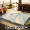 A glass cutting board featuring a Seneca Lake map and compass design sits on a wooden dock.