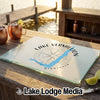 A rectangular glass cutting board featuring a Lake Vermilion, Minnesota map and compass design sits on a wooden dock.