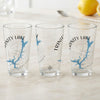 Three clear glasses display "TRINITY LAKE CALIFORNIA" with a blue lake map and compass.