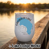 A white stemless wine tumbler with a blue map of Garibaldi Lake sits on a wooden dock at sunset.