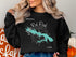 Black sweatshirt with a turquoise map of Lake Red Rock, Iowa, and compass rose.