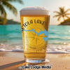 Beer glass with "Actola Lake" and compass design on a beach with palm trees.