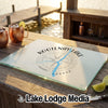 A rectangular glass cutting board featuring a Kootenay Lake Canada map graphic rests on a wooden dock.