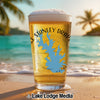 Beer glass with a blue Oklahoma map graphic, on a beach with palm trees.