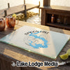 A rectangular glass cutting board rests on a wooden dock with copper mugs and lime wedges.