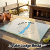 A tempered glass cutting board featuring a Torch Lake, Michigan map graphic rests on a wooden outdoor bar.