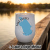 A white stemless wine tumbler with a blue map of Lake George, Florida, resting on a wooden dock at sunset.