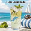 Glass with beverage, limes, mint, and Lake Lodge Media logo on beach.