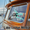 Sticker "Hebgen Life" on wooden boat window, with Lake Lodge Media logo below.