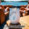 A white wine tumbler with a compass and lake design sits on a wooden boat table.