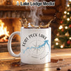 White mug with Fort Peck Lake Montana design, splashing coffee, by fireplace and Christmas tree.