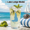 Glass with drink, lime, mint, and sunglasses on beach with sailboat.